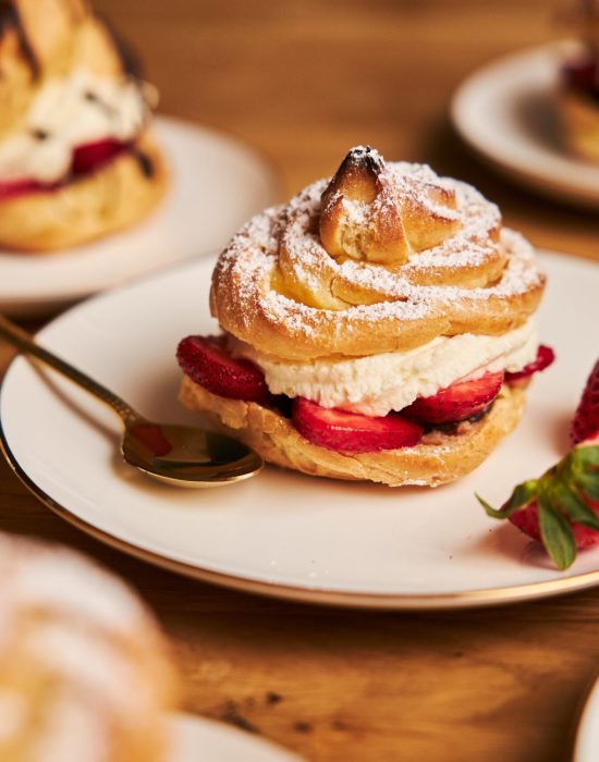 A closeup shot of delicious cream puff with strawberries on a wooden table